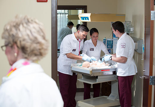 Three student nurses in simulated hospital setting caring for infant.